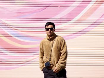 Young man wearing sunglasses while standing against wall