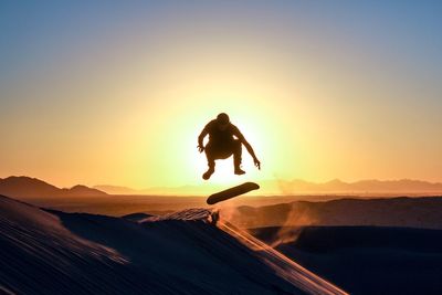 Man performing stunt while sandboarding during sunset