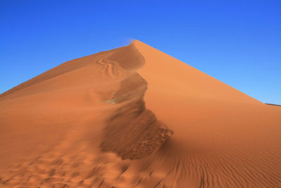 Low angle view of sand dunes against clear blue sky