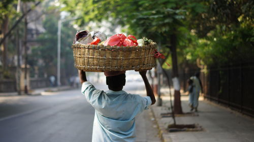 Rear view of man carrying vegetables in basket on street