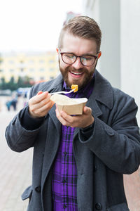 Portrait of young man holding ice cream standing outdoors