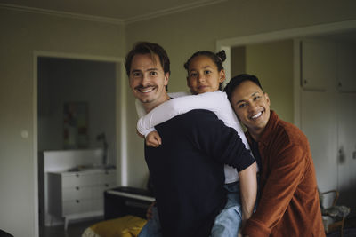 Portrait of gay couple piggybacking daughter at home