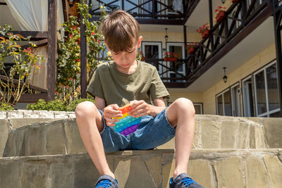 Serious and concentrated boy playing popit toy outdoors, in the yard of a small guest house.