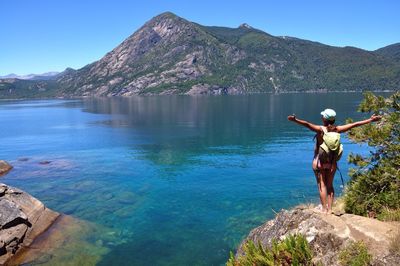 Rear view of hiker standing at lakeside with arms outstretched