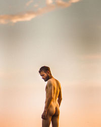 Rear view of naked man standing against sky during sunset