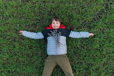 Smiling teen boy lies on green grass with his arms