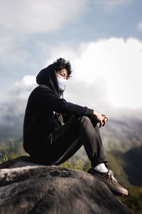 Man sitting on rock against sky