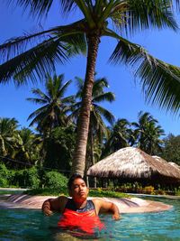 Young man looking away while relaxing in swimming pool against sky