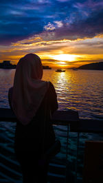 Woman looking at sea against sky during sunset