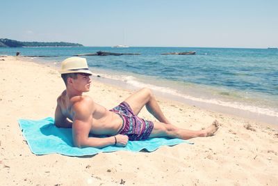 Shirtless man relaxing at beach against clear sky