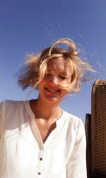 Low angle view of smiling beautiful woman by hooded beach chair against clear blue sky