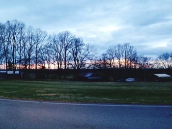 Bare trees on field against cloudy sky