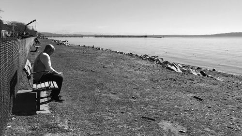 Full length of man sitting on seat at beach against sky