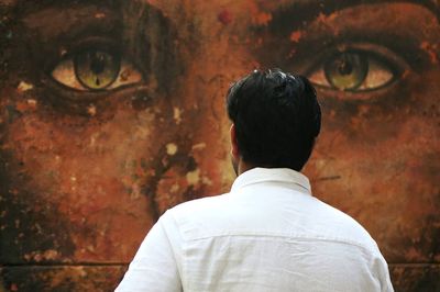 Rear view of man looking away against wall