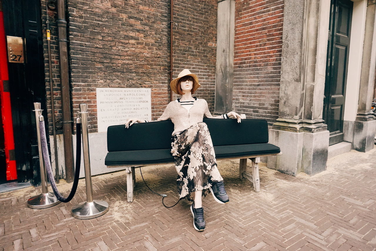 PORTRAIT OF YOUNG WOMAN SITTING ON CHAIR IN FRONT OF BUILDING