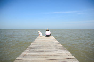 Rear view of woman with child sitting on pier over sea