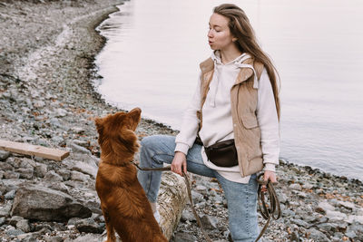 Young woman and dog retriever walks on river shore at autumn season