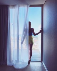 Rear view of woman standing by window at home