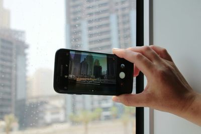 Midsection of man photographing through smart phone on window