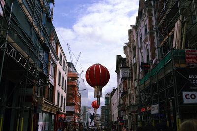 Low angle view of lanterns hanging amidst buildings against cloudy sky in city