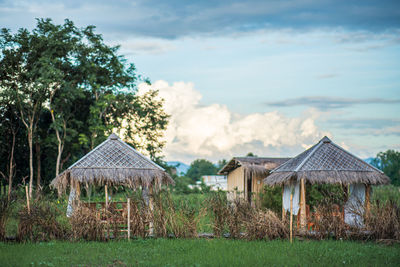 Houses by trees on field against sky