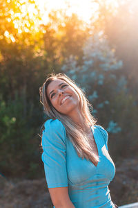 Smiling young woman standing in forest at sunset