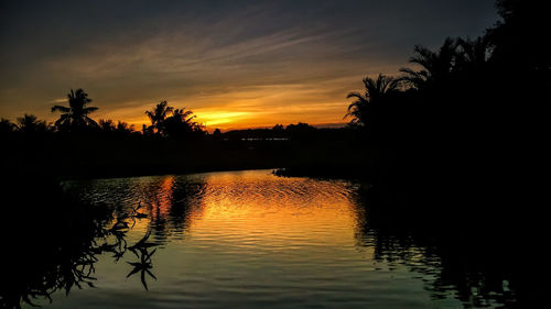 Silhouette trees by lake against sky during sunset