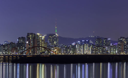 Illuminated modern buildings in city against sky at night