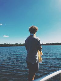 Rear view of man standing by lake against sky