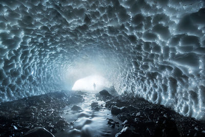 Distant view of man standing on rocks in ice covered cave