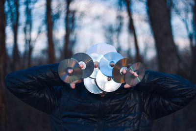 Man holding compact discs against his face in forest