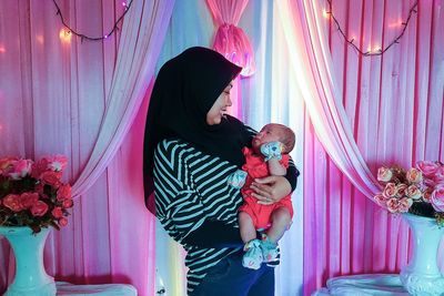 Smiling mother with toddler against illuminated curtain