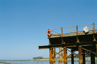 Low angle view of life belt on pier over sea against clear sky