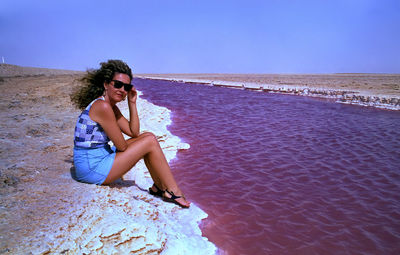 Young woman sitting on sunglasses against clear sky