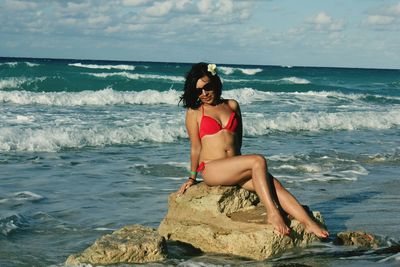 Full length of sensuous woman in bikini relaxing on rock at beach