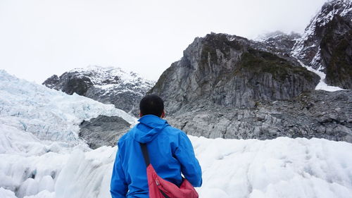 Rear view of man standing on snowcapped mountain against sky