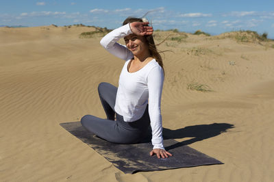 Beautiful woman with yoga mat sitting on dunes