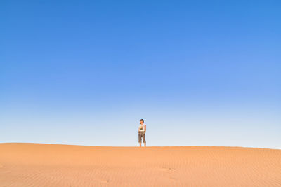 Woman standing on desert against clear blue sky