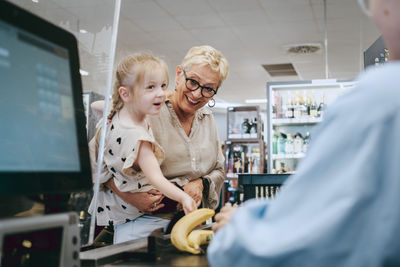 Happy senior woman with granddaughter near checkout at supermarket