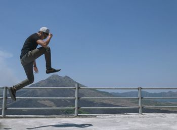 Full length side view of young man jumping at observation point with gunung batur in background