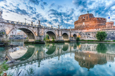 Arch bridge over river against cloudy sky