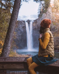 Rear view of young woman sitting against waterfall