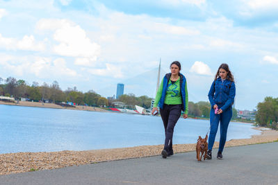 Mother and her teen girl walking with pinscher dog by the of relationship between human and animal.