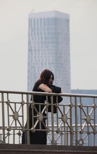 Woman standing on bridge against skyscraper in city