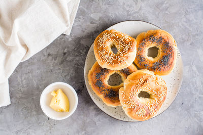 Bagels with poppy seeds and sesame seeds on a plate and butter in a bowl on the table. 