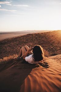 Rear view of young woman lying on sand at desert against sky