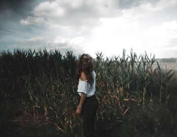 Young woman standing on field against sky