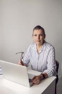 Woman in a white striped shirt aged sits at a computer at home with glasses