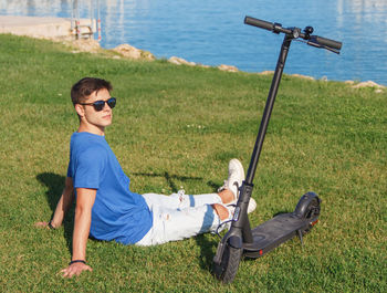 Young caucasian man sitting on grass near electric scooter