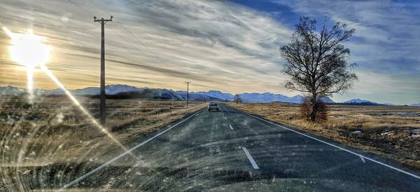 Road by bare trees on field against sky